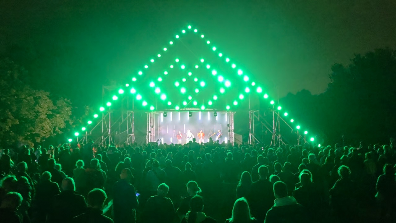 Scena su apšvietimu, choras scenoje ir žiūrovai renginio aikštėje