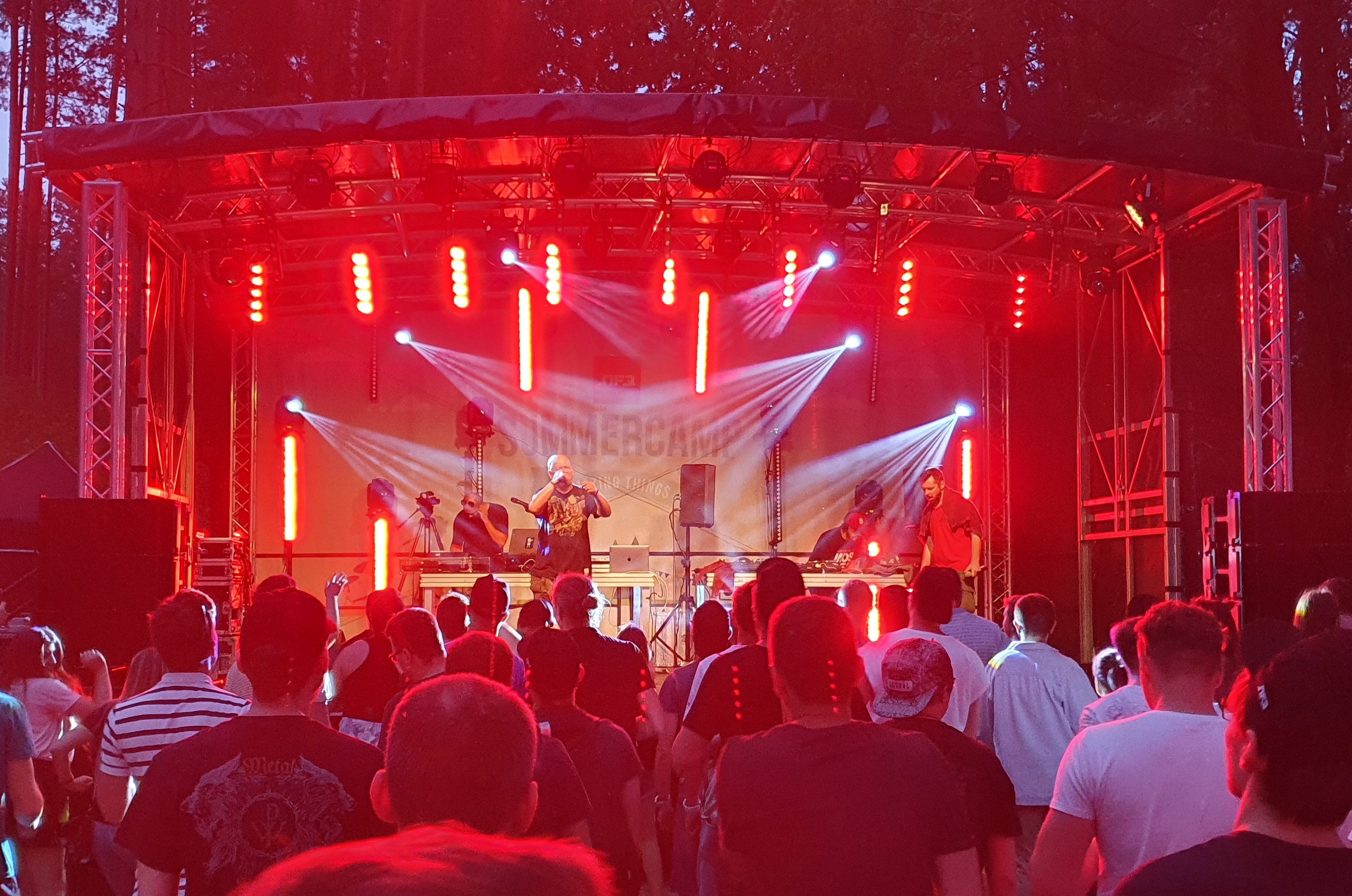 Scena su apšvietimu, choras scenoje ir žiūrovai renginio aikštėje